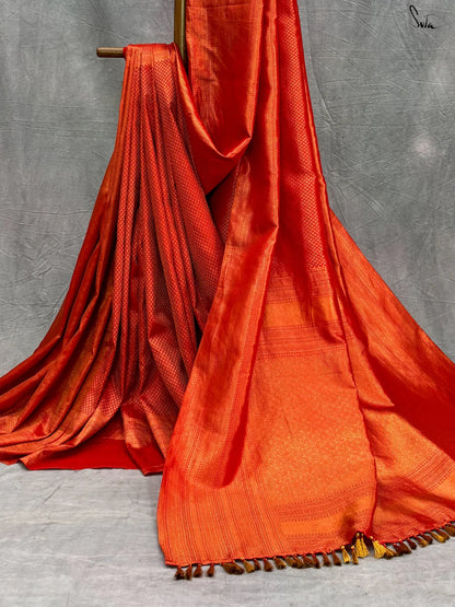 Red silk saree with gold zari on a textured pattern on a gray background