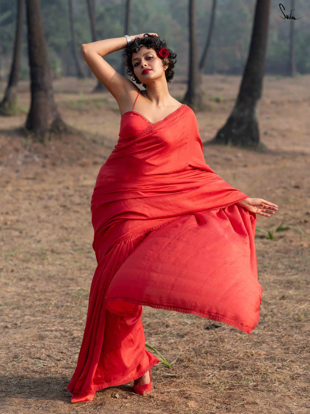Woman in a red silk saree standing in a forested area