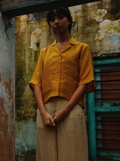 Person wearing a yellow shirt and beige pants standing against a textured wall.