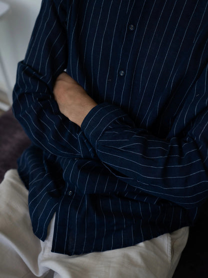 Person wearing a dark blue pinstripe shirt with a white garment underneath.