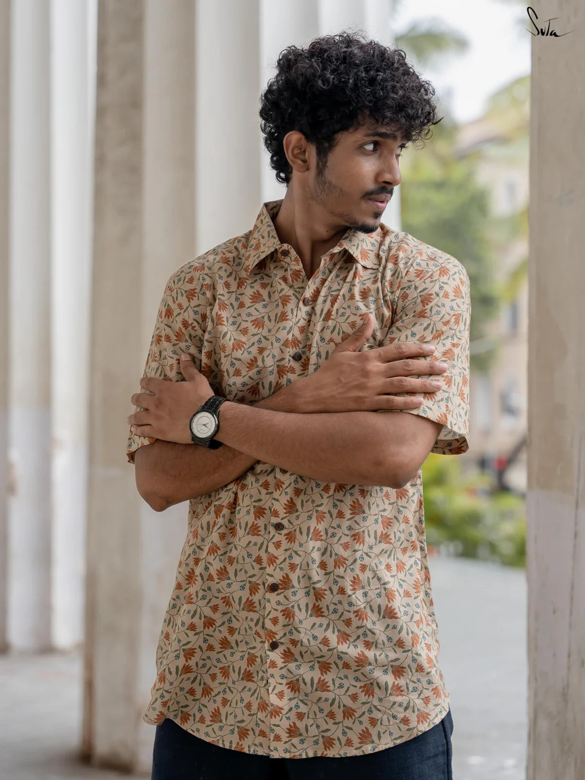 Man wearing a beige floral patterned shirt standing outdoors with columns in the background