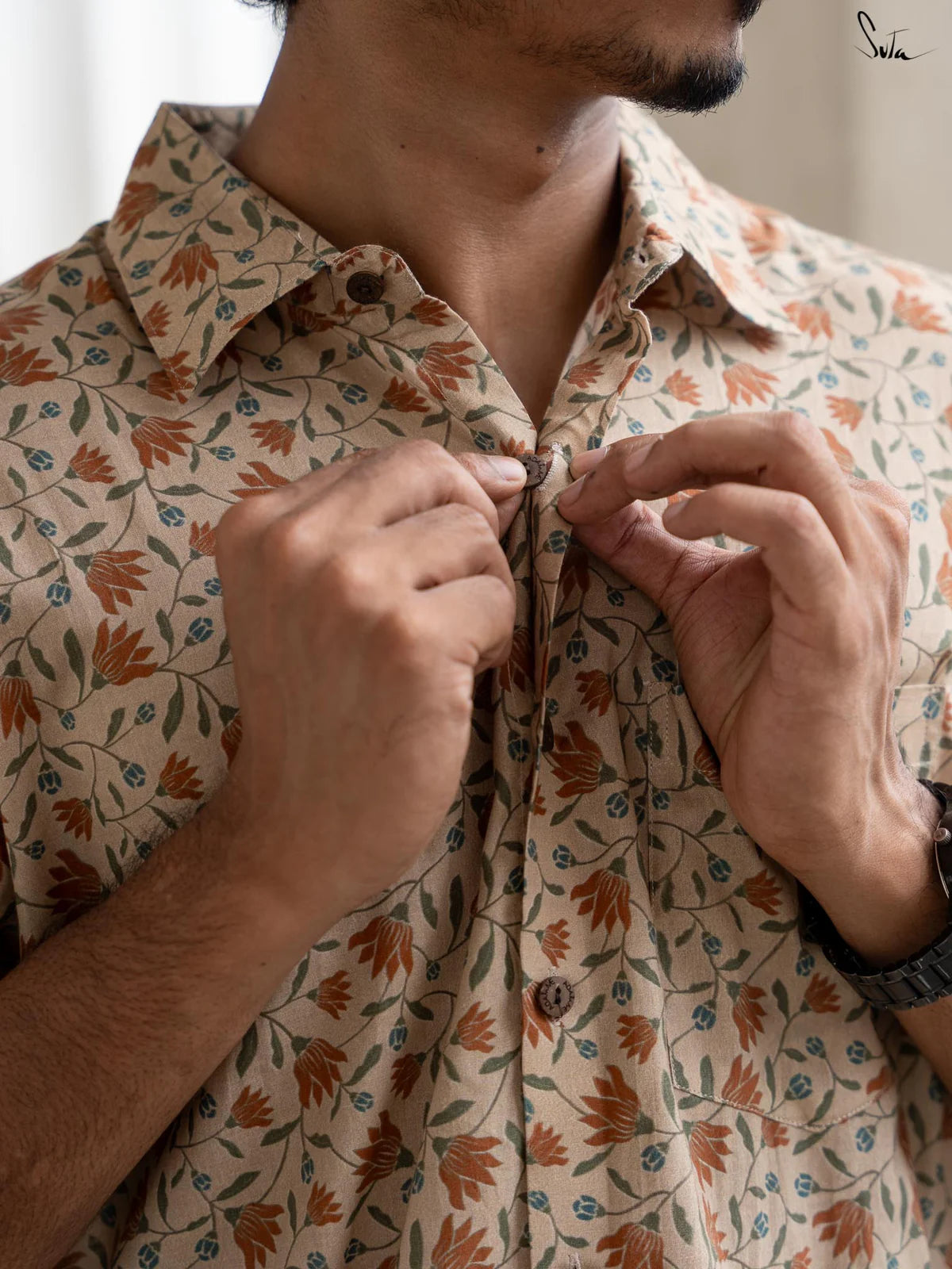 Person wearing a floral patterned shirt buttoning their collar.
