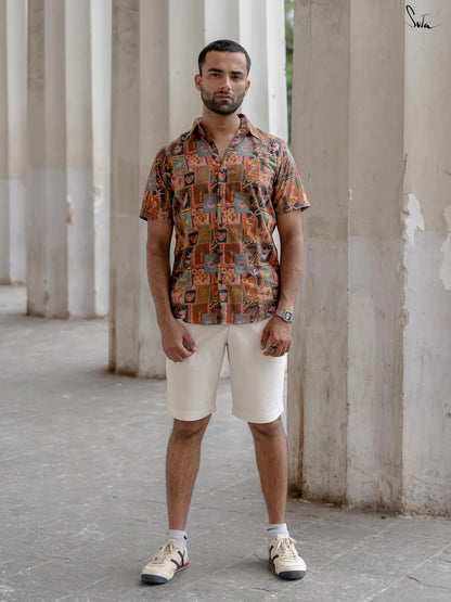 Man wearing a multicolored patterned shirt and beige shorts standing in an outdoor setting with columns.