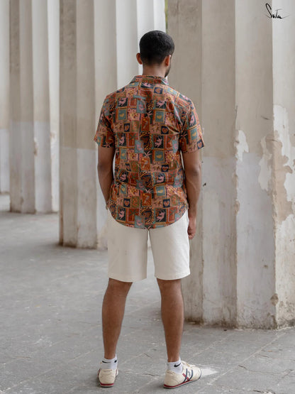 Man wearing a patterned shirt and beige shorts standing in an outdoor setting with columns.