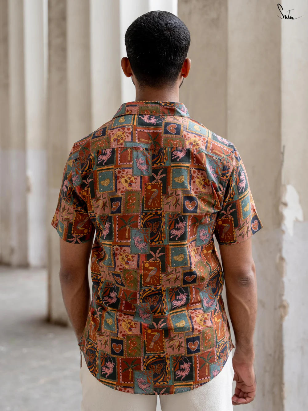 Person wearing a patterned shirt standing in front of classical columns.