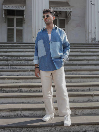 Man wearing a blue patterned shirt and white pants standing on steps.