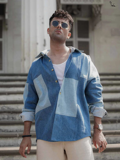 Man wearing a blue patterned shirt and sunglasses standing on steps.