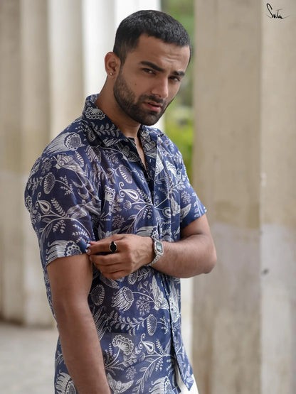 Man wearing a blue patterned shirt standing outdoors with columns in the background