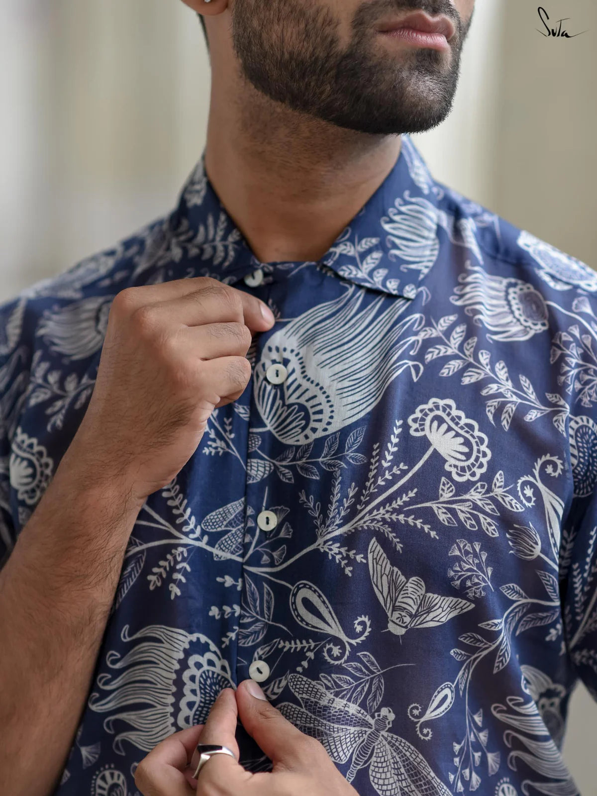 Close up of a man wearing a blue floral patterned shirt with a blurred background