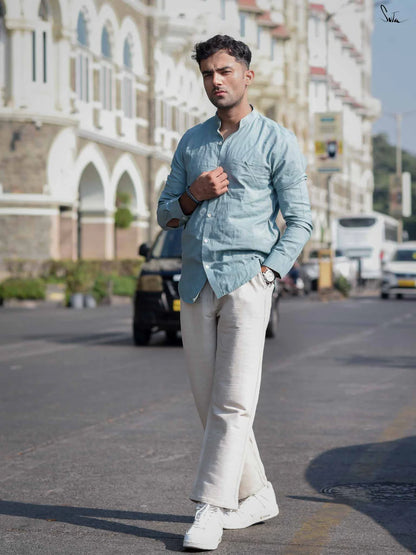 Man walking on a street wearing a light blue shirt and white pants.