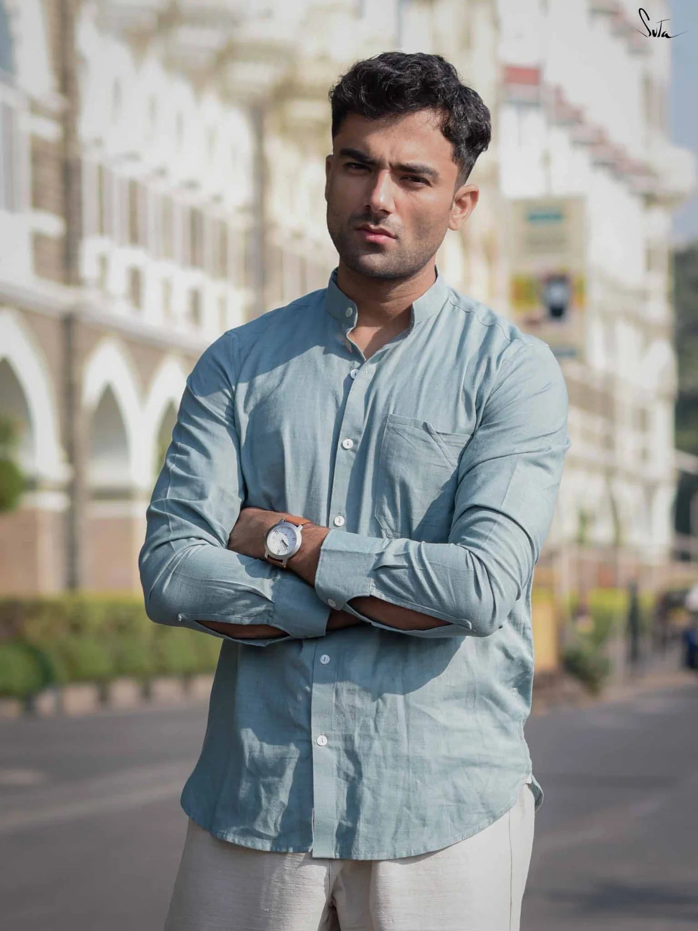 Man wearing a light blue shirt with arms crossed in an outdoor setting