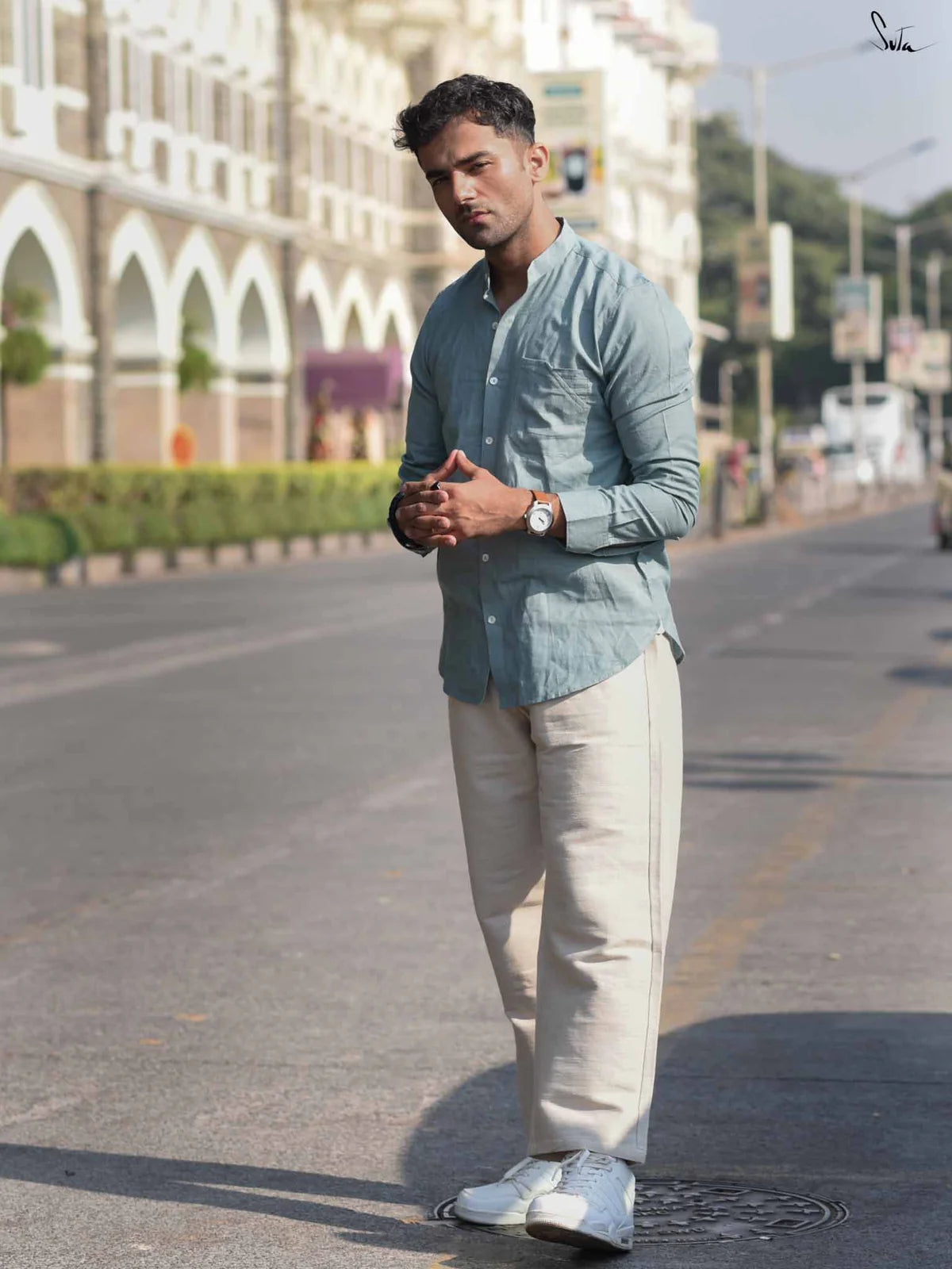 Man in light blue shirt and beige pants standing on a street with buildings in the background