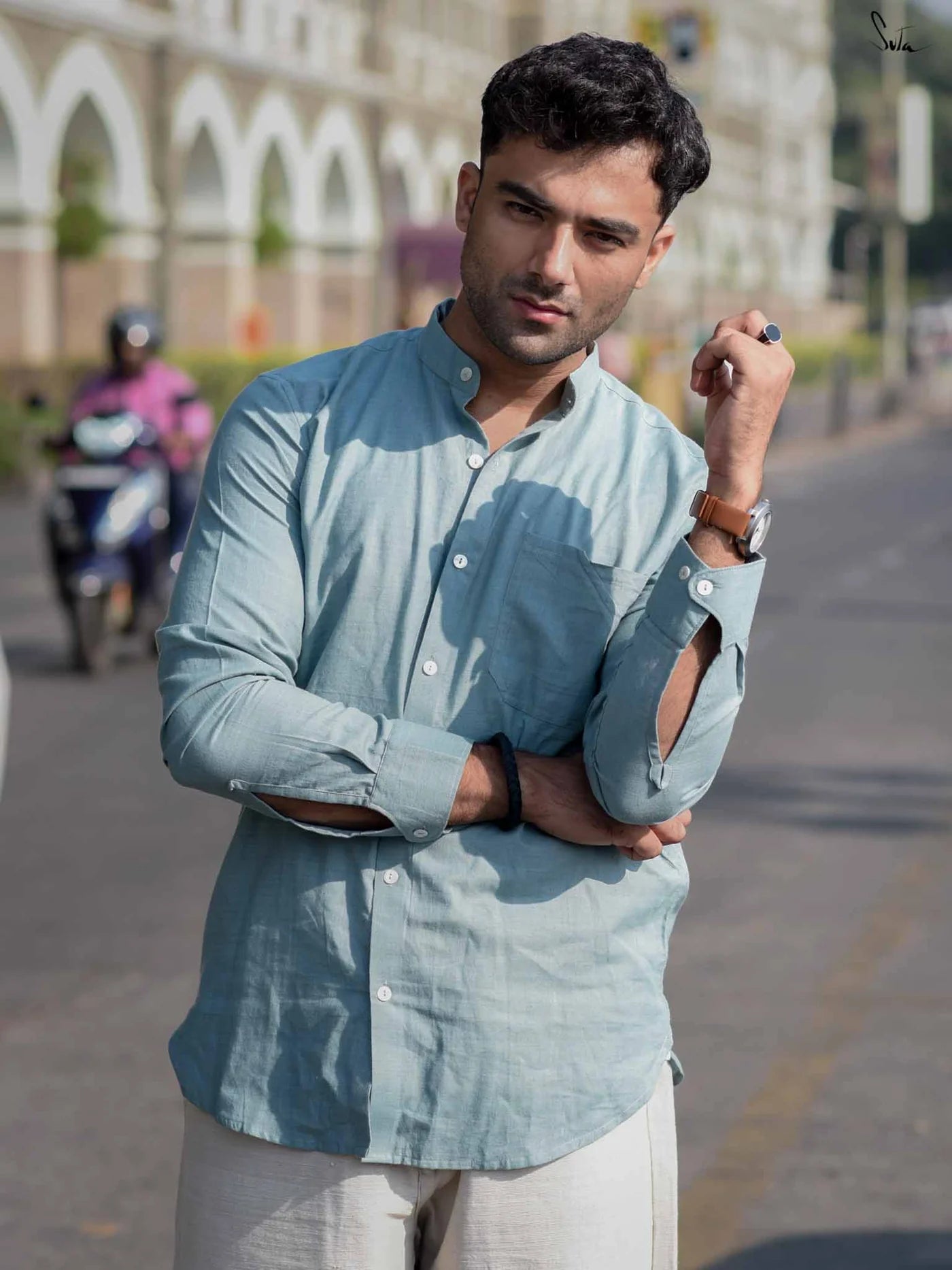 Man in a light blue shirt standing on a street with a blurred background