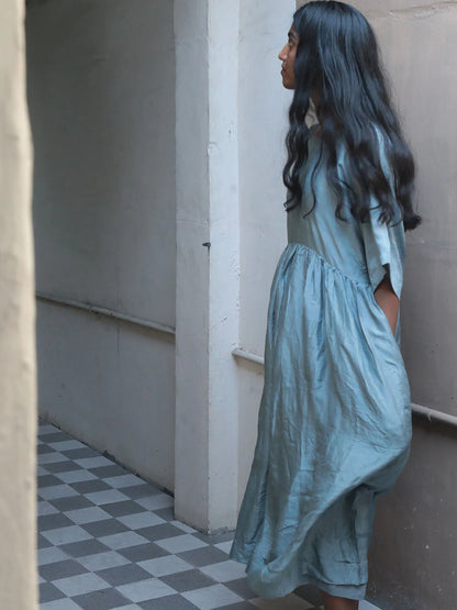 Woman in a blue dress standing in a narrow hallway with checkered floor.
