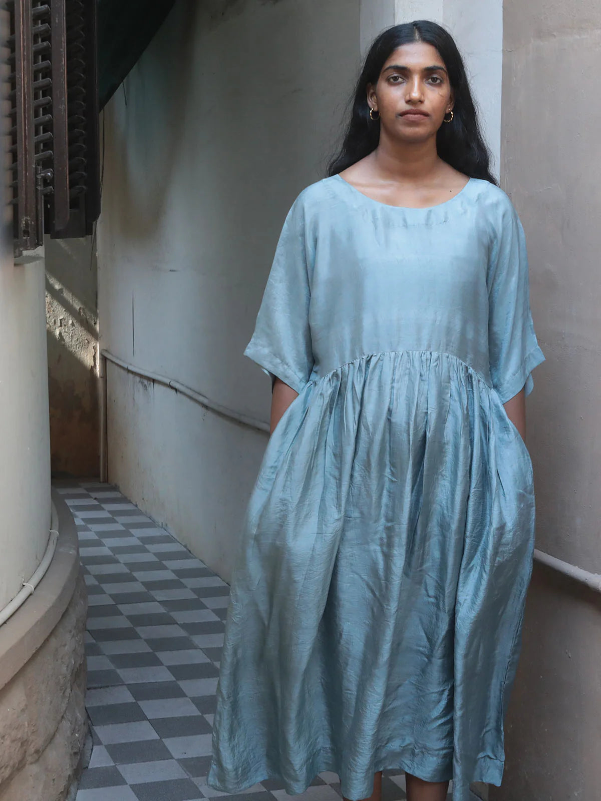Woman wearing a light blue dress standing in an alleyway.
