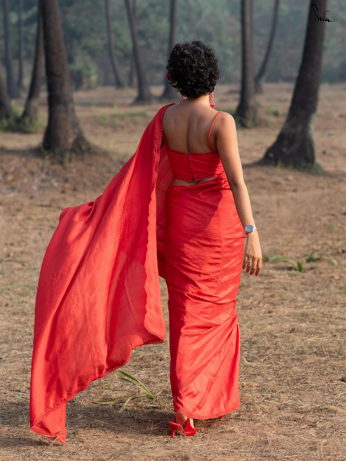 Woman in a red saree walking away in a forested area