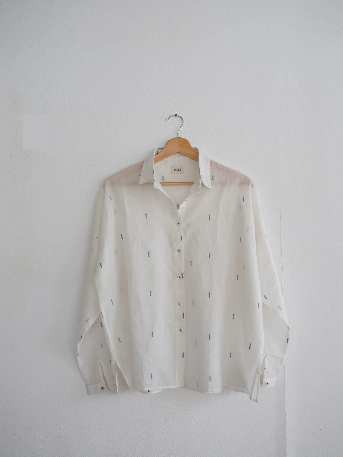 White shirt with subtle blue patterns on a wooden hanger against a white background