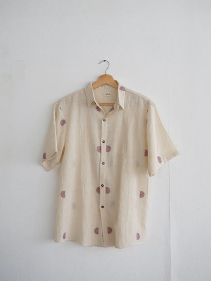 Beige shirt with small red patterns on a hanger against a white wall