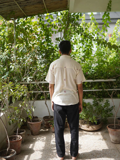 Person in beige shirt with half moon red pattern tending to plants on a balcony with buildings in the background