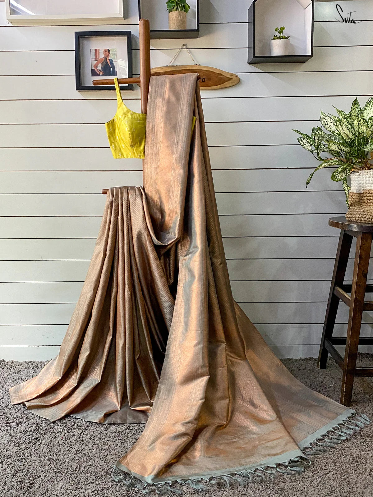 Gold saree draped over a wooden rod with a yellow top in the background on a wooden wall.