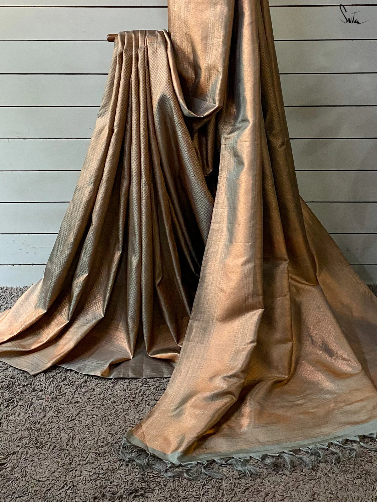 Gold-colored saree fabric draped over a surface with a wooden panel background