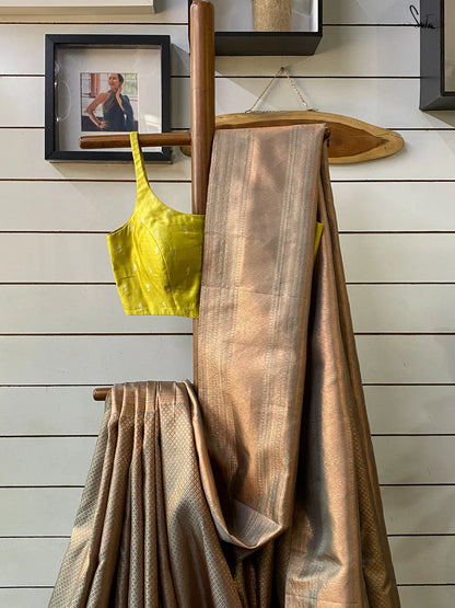 Gold saree draped over a wooden rod with a yellow top in the background on a wooden wall.