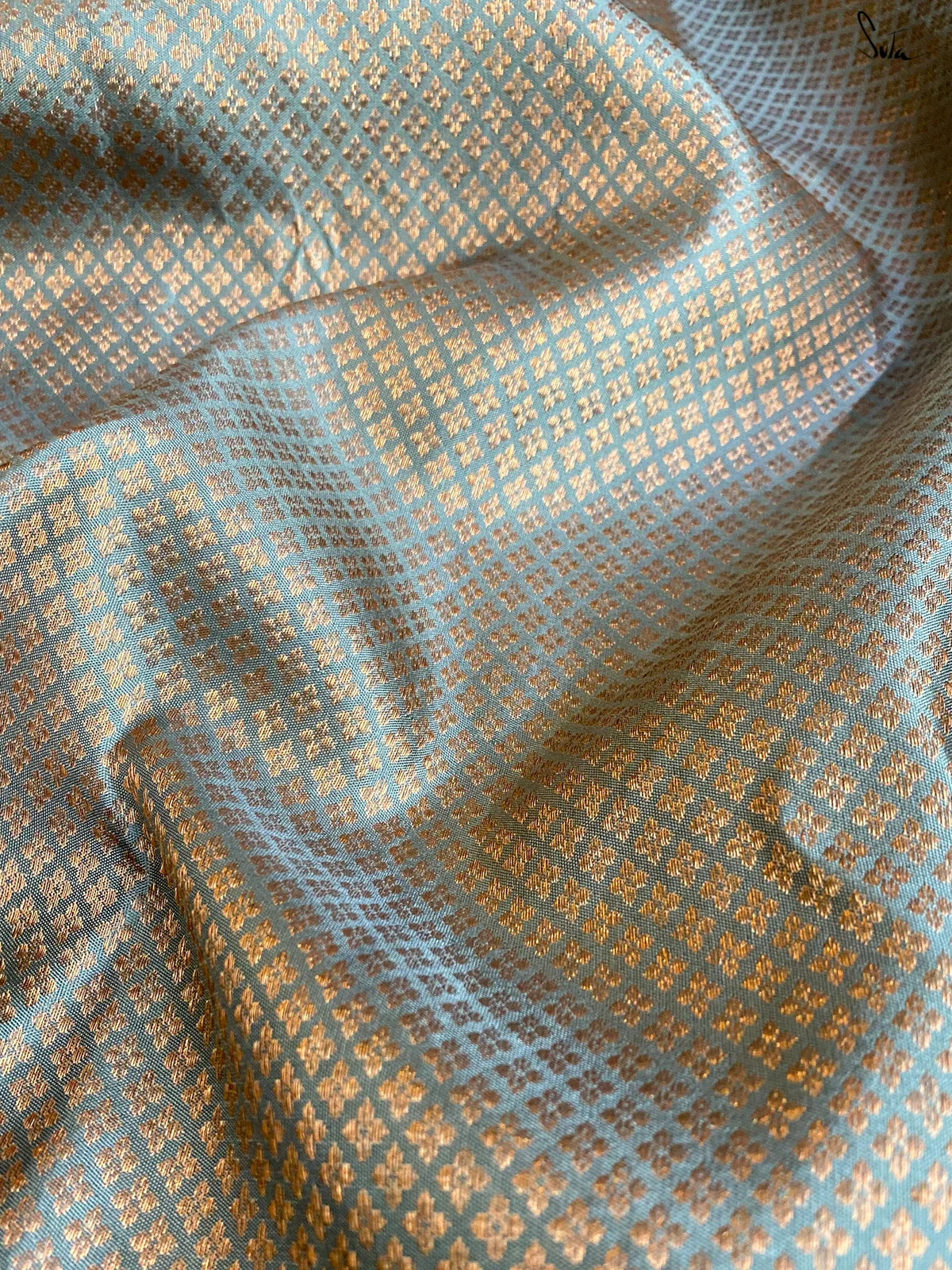 Textured gold fabric with a subtle pattern on a light blue background