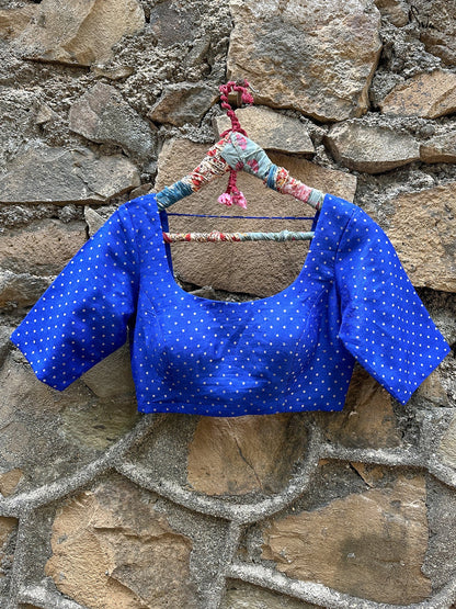 Blue polka dot blouse on a floral hanger against a stone wall