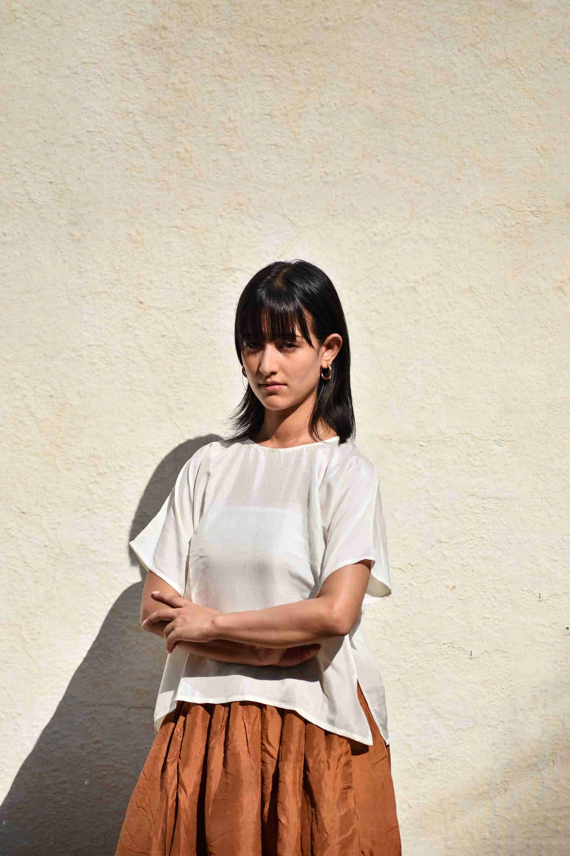 Woman wearing a white top and brown skirt against a textured beige wall