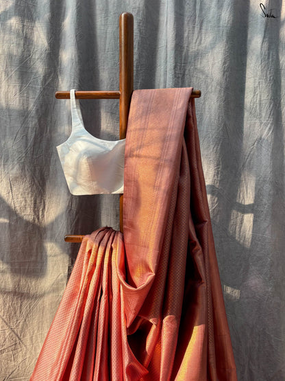 Red and Gold saree fabric draped over a wooden stand against a textured wall.