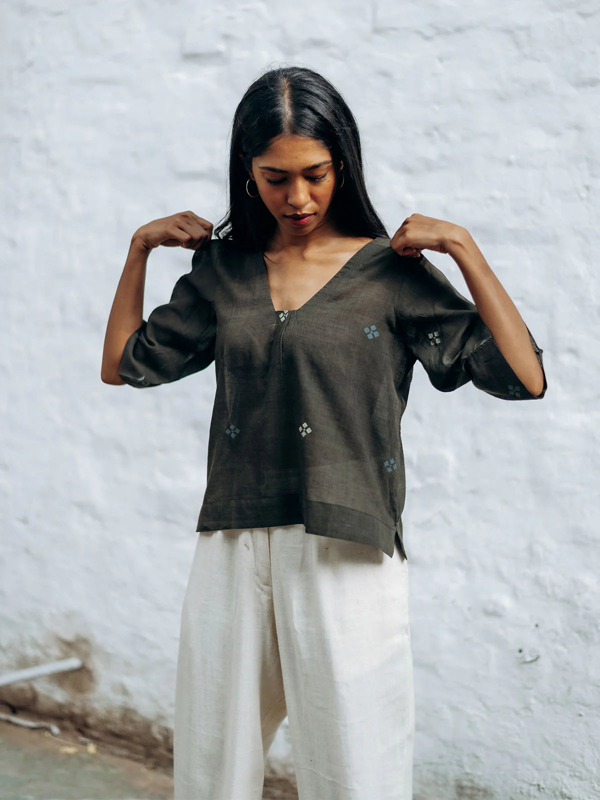 Woman wearing a gray blouse with floral patterns against a textured white wall.