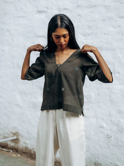 Woman wearing a gray blouse with floral patterns against a textured white wall.