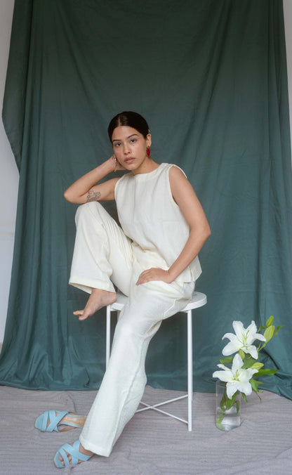 Woman in a white outfit sitting on a chair with a green curtain background