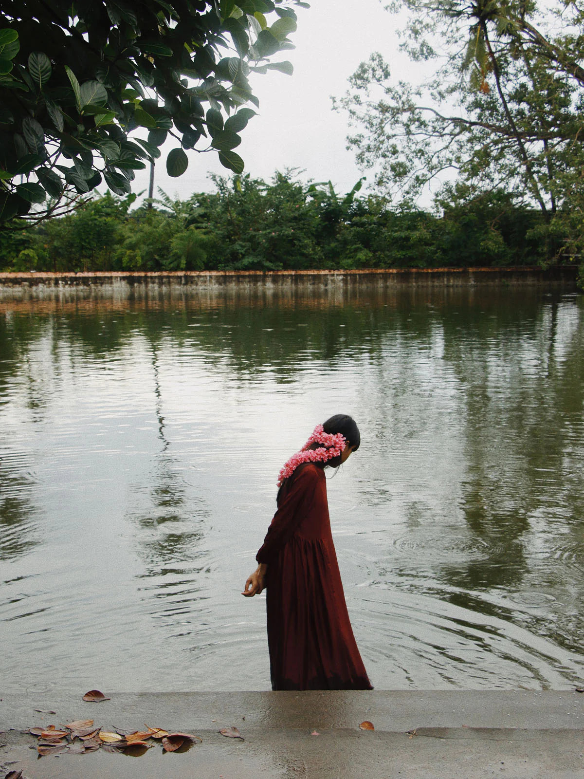 Person in a long dark red dress standing in water with trees in the background