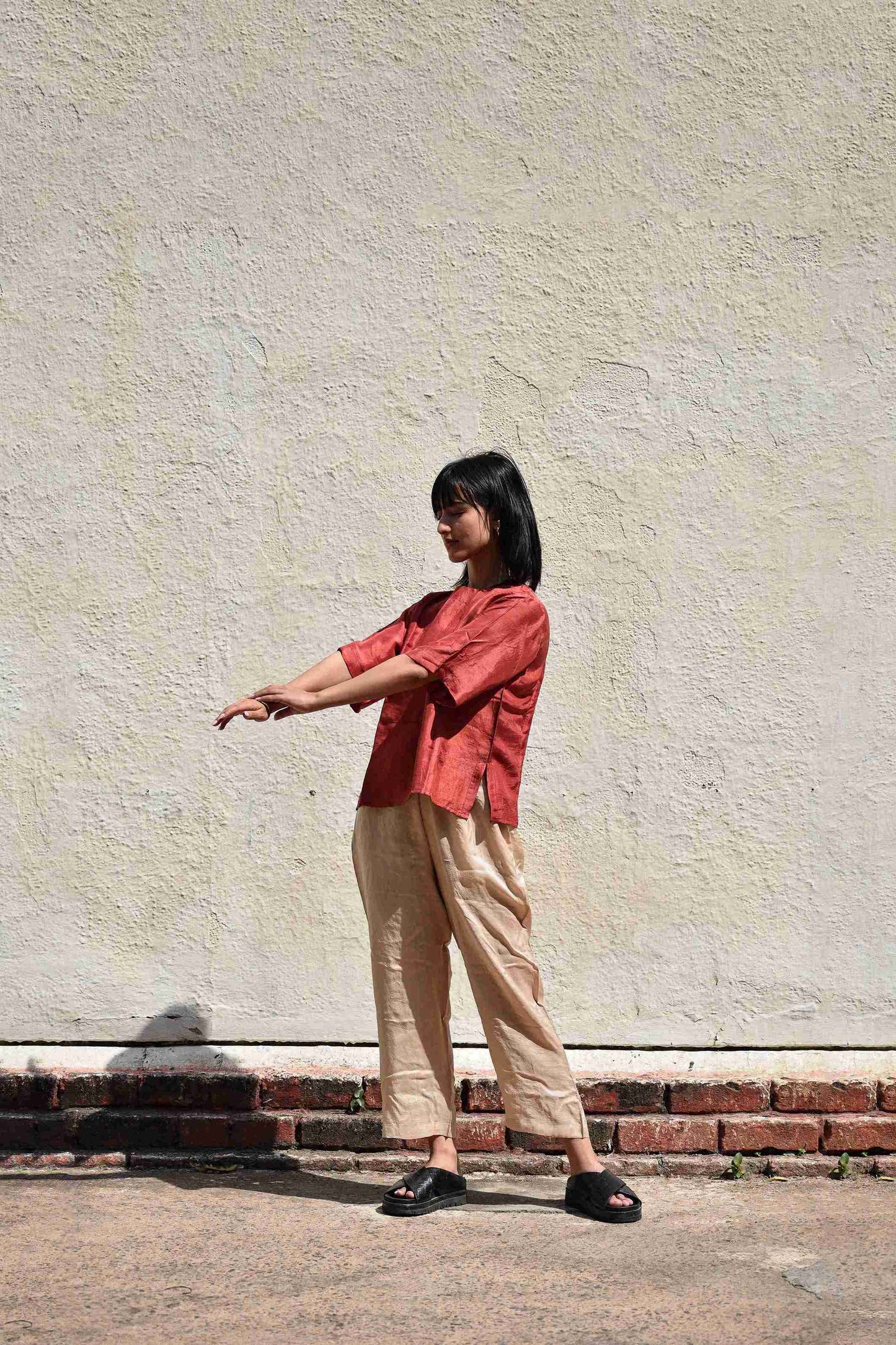 Person wearing a red shirt and beige pants standing against a light-colored wall.
