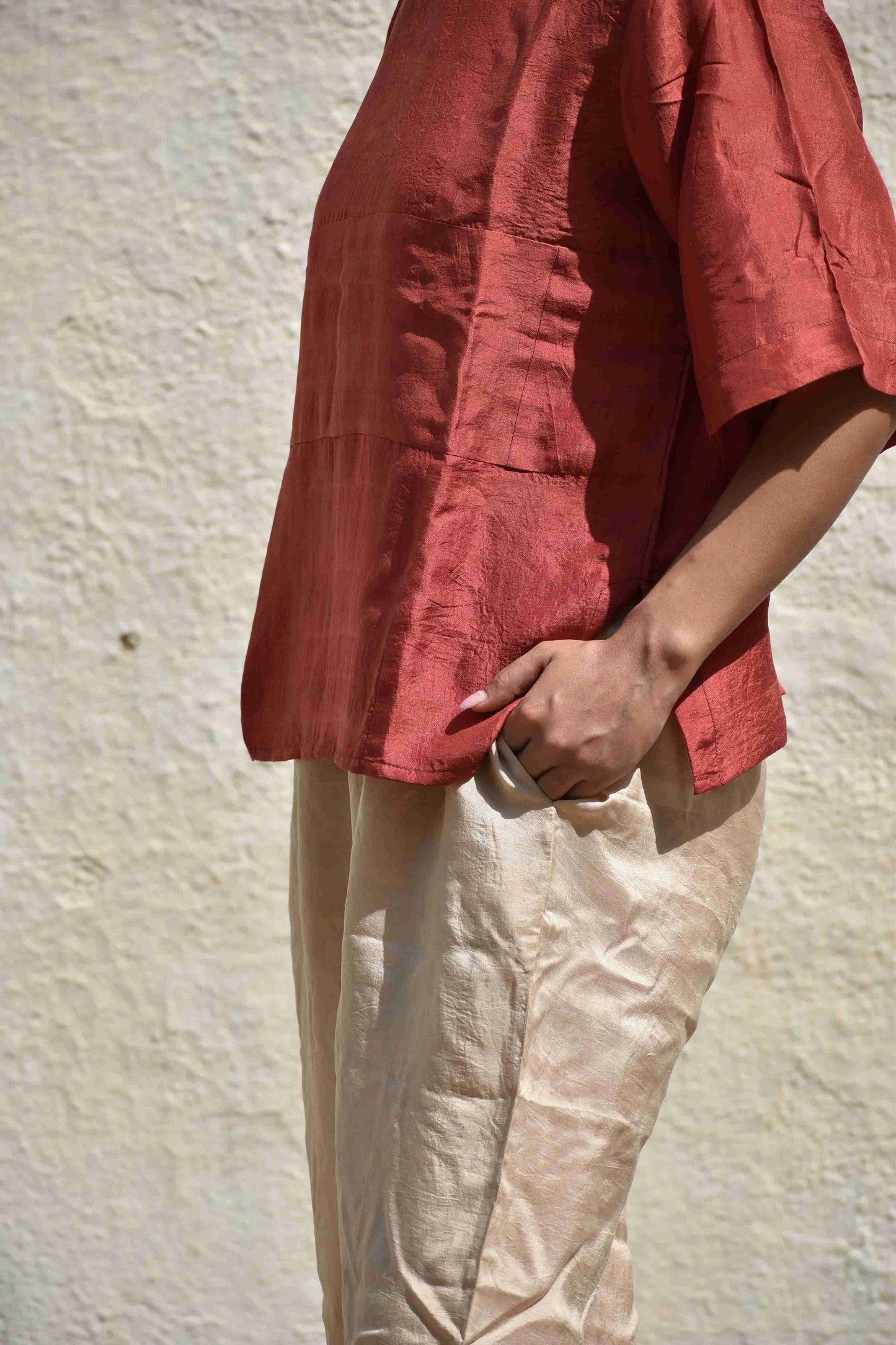Person wearing a red shirt and beige pants against a textured wall.