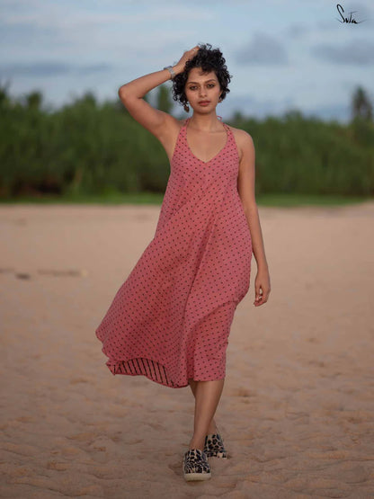 Woman in a pink dress standing on a beach with greenery in the background