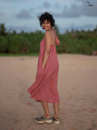 Woman in a pink dress standing on a sandy beach with greenery in the background