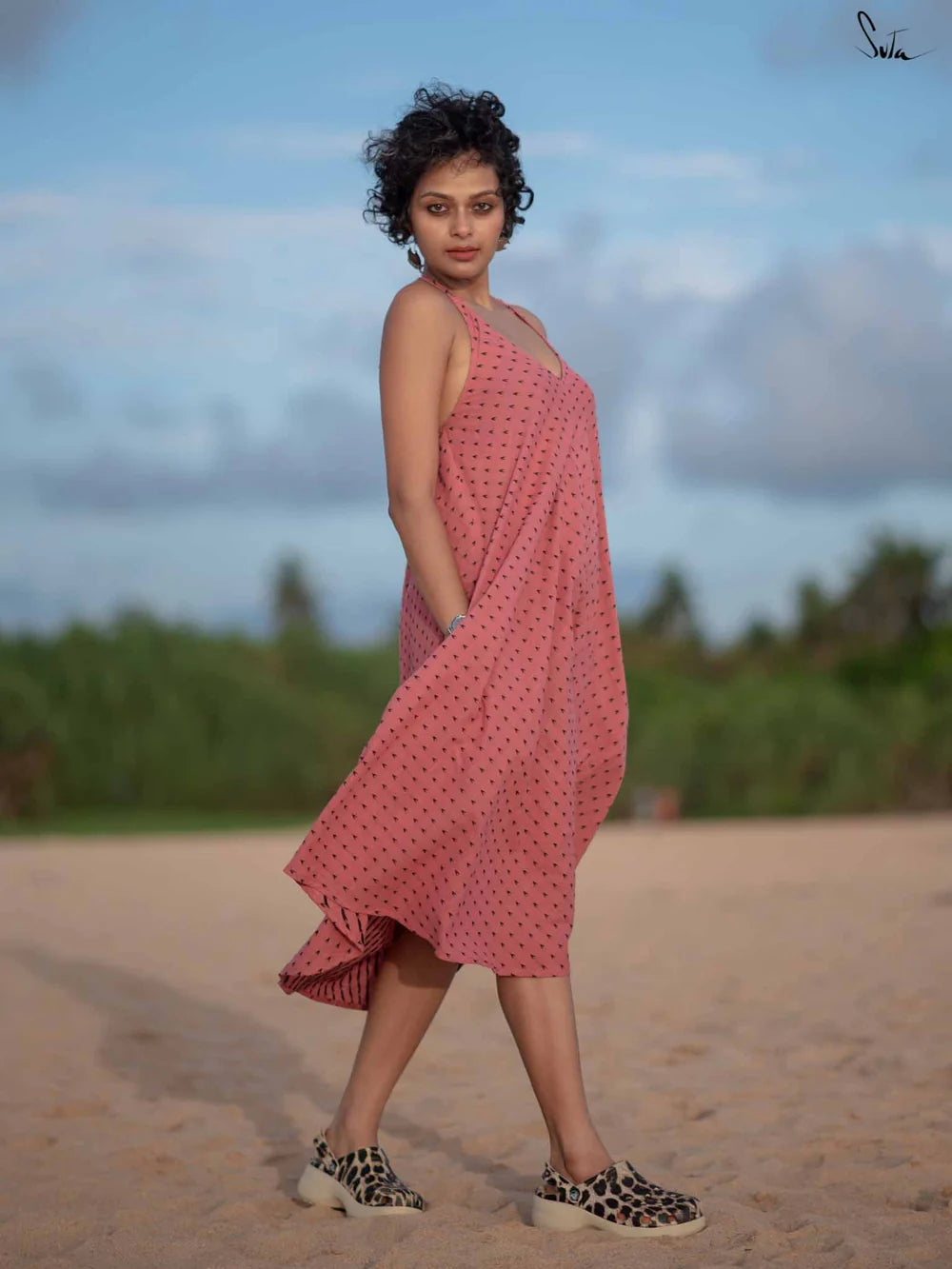 Woman in a pink dress standing on a beach with a blurred natural background