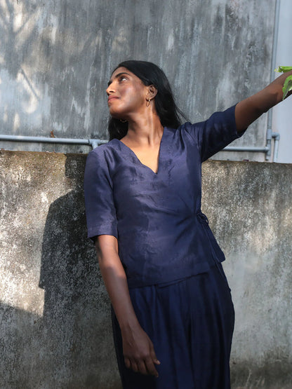 Woman in a navy blue outfit standing against a textured wall.