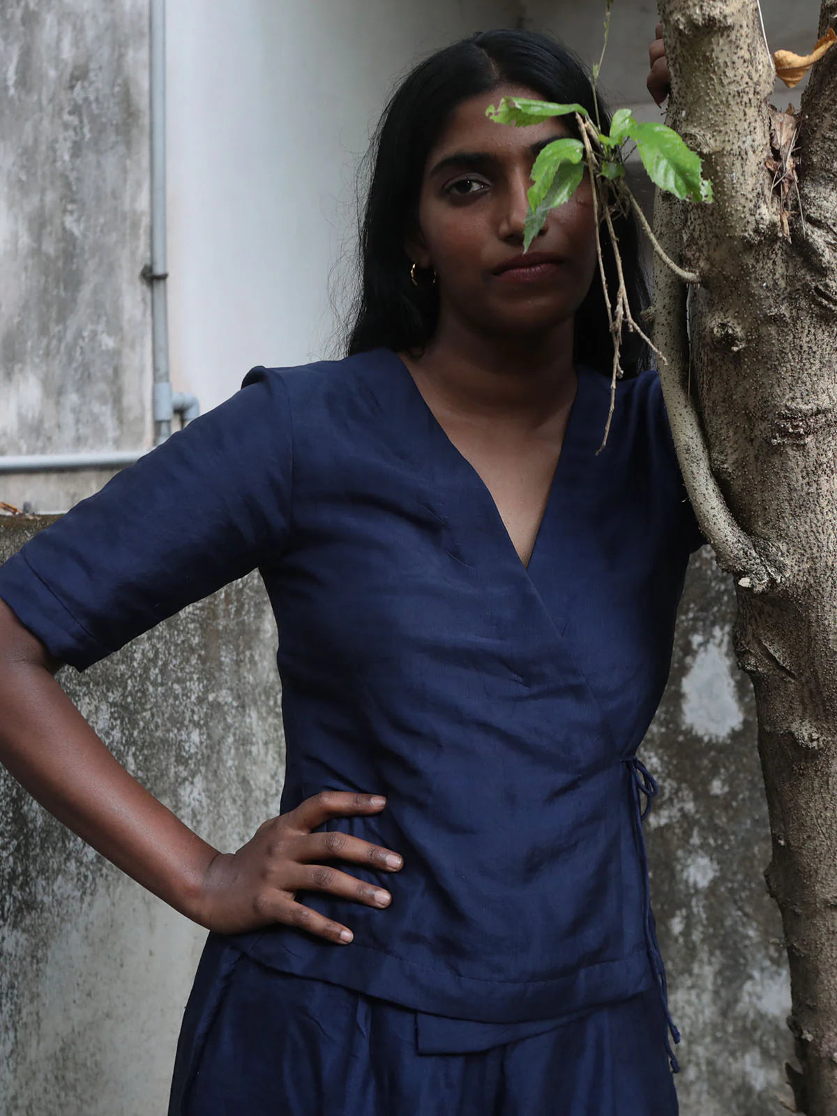Woman in a blue outfit standing against a textured wall with a plant.