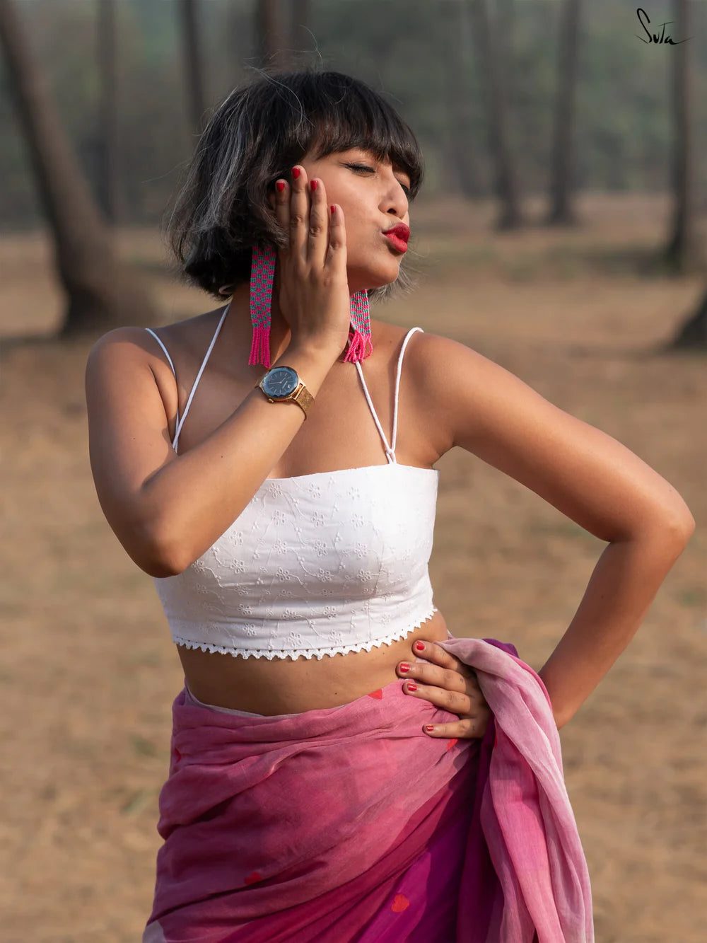 Woman in a white blouse and pink saree standing outdoors with trees in the background