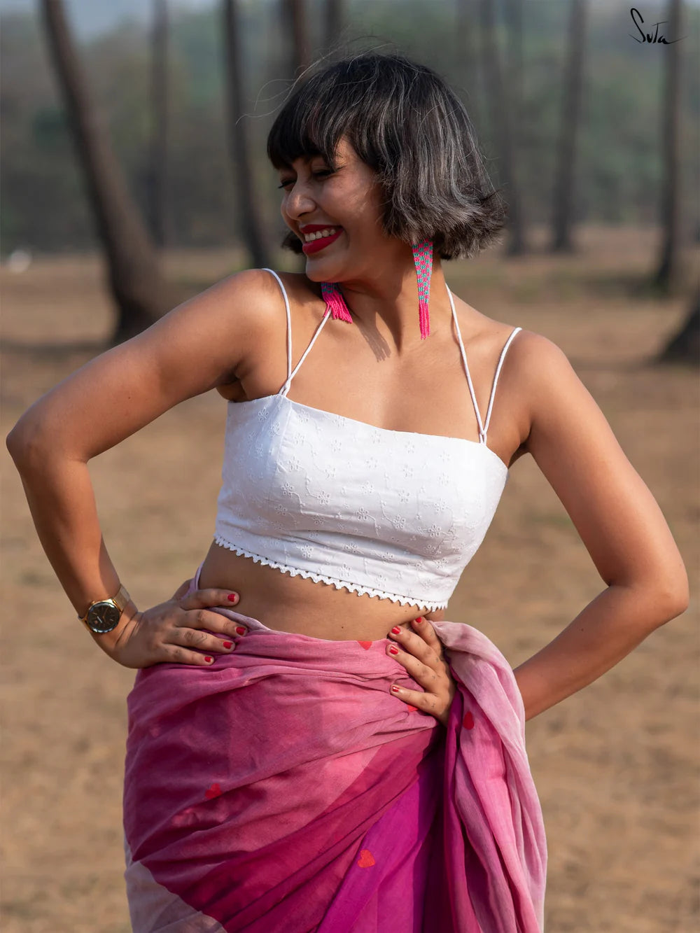 Woman in a white blouse and pink saree standing outdoors with trees in the background