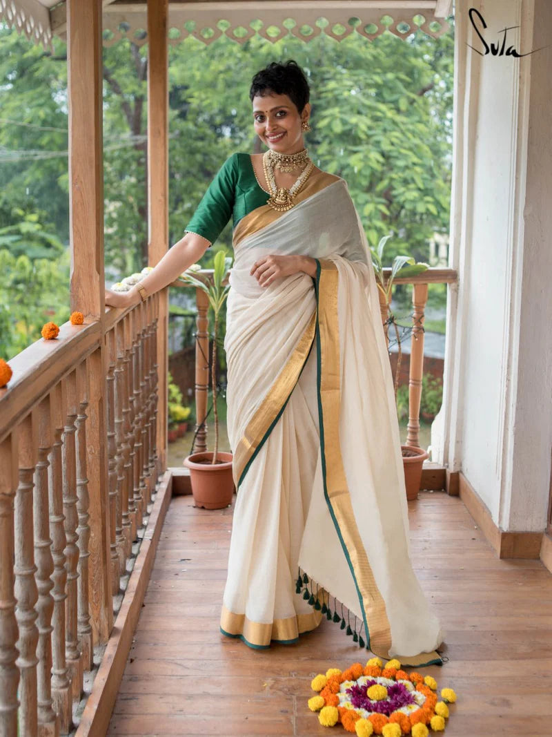 Woman in a white saree with gold border on a balcony