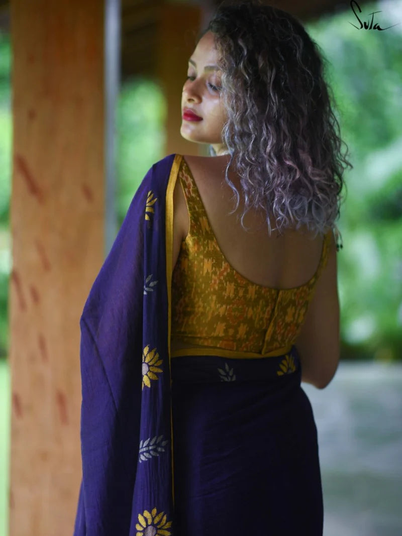 Woman wearing a yellow blouse and purple saree with ikat patterns, standing outdoors.
