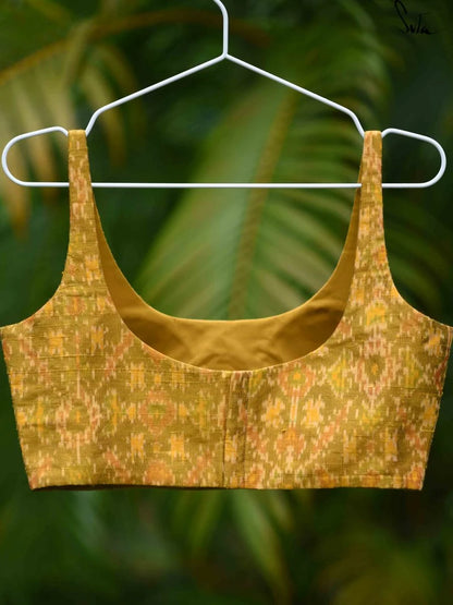 Yellow silk ikat blouse on a hanger against a blurred green background