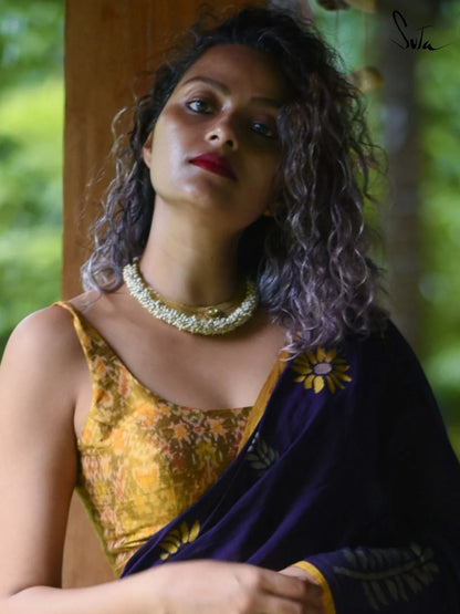 Woman wearing a saree and yellow ikat blouse with a necklace, standing outdoors.