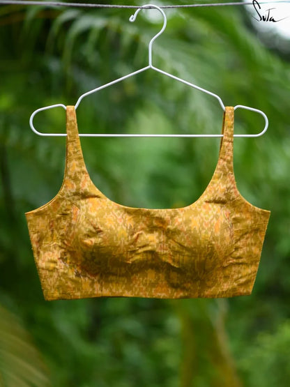 Yellow silk ikat blouse on a hanger against a blurred green background
