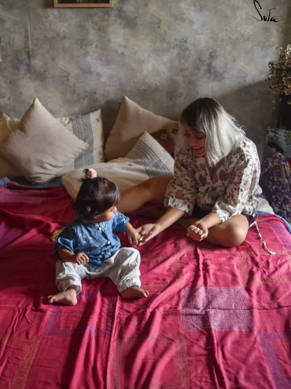 Woman and child sitting on a quilt with a textured wall background