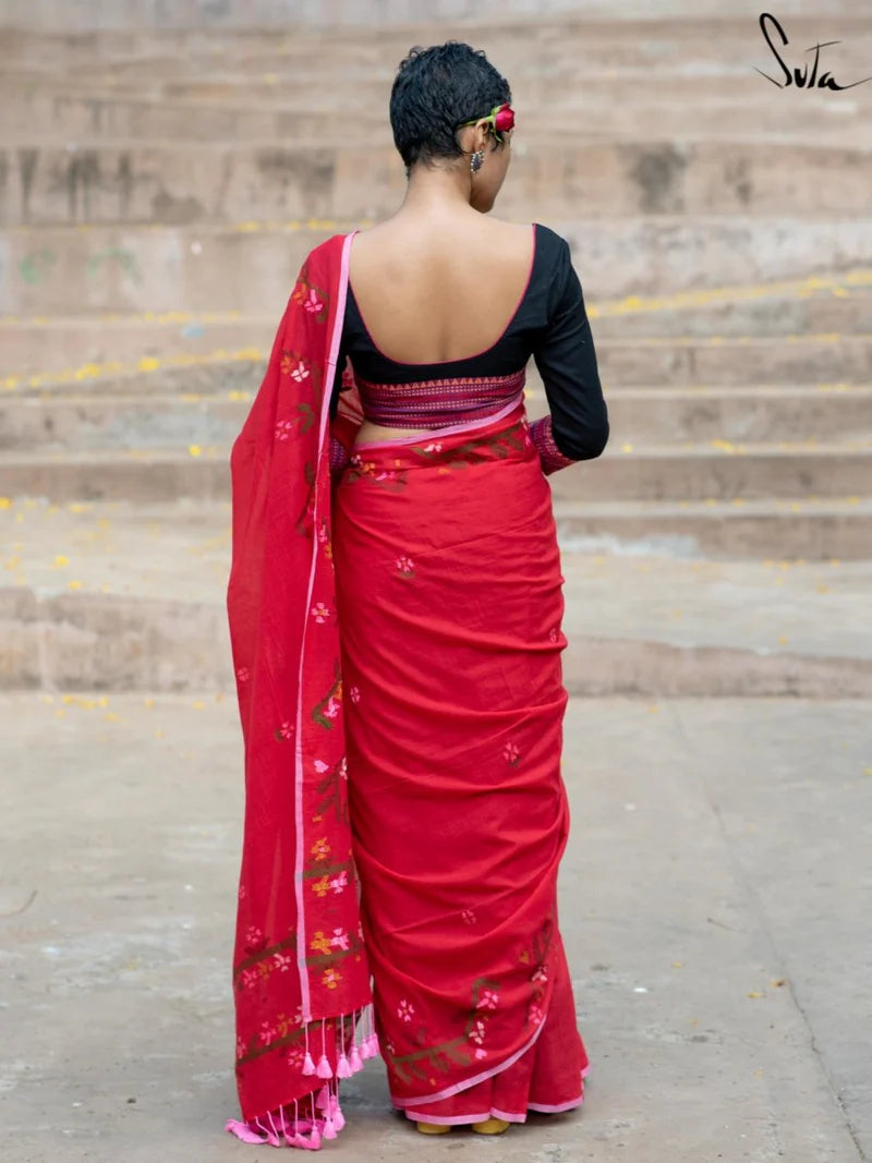 Person wearing a red saree with a black blouse standing on steps.